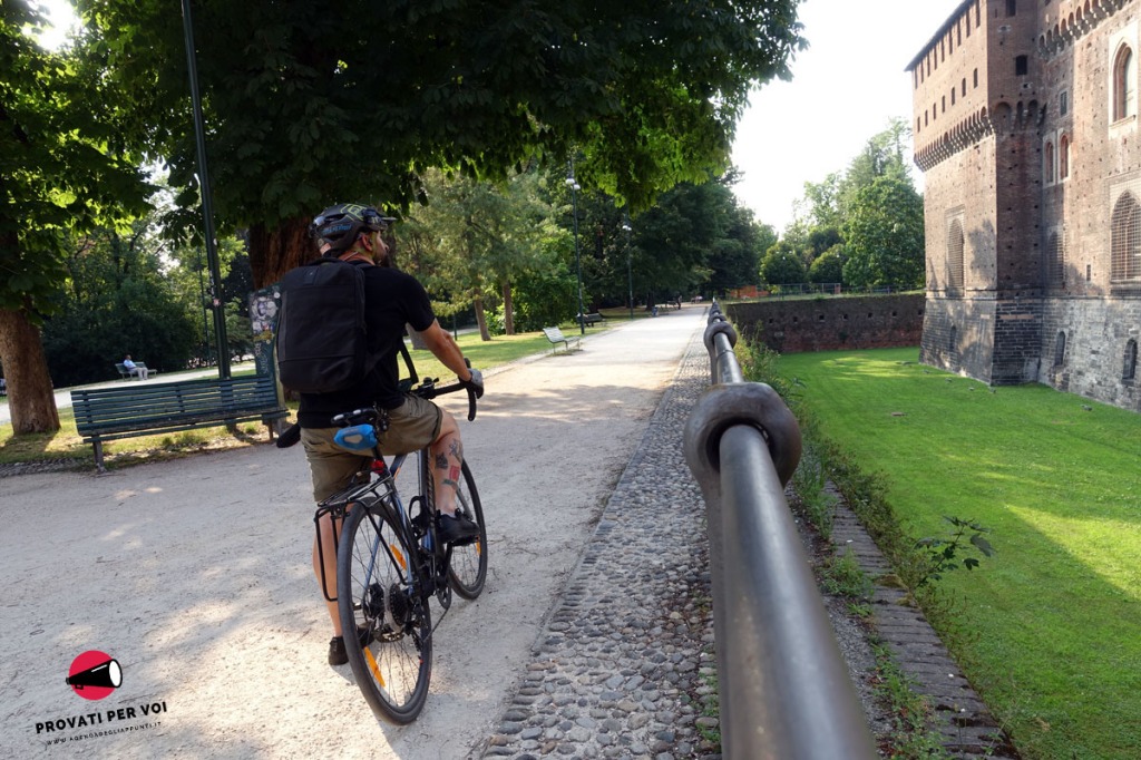 un ciclista in sella alla sua gravel bike è fermo al castello sforzesco di milano