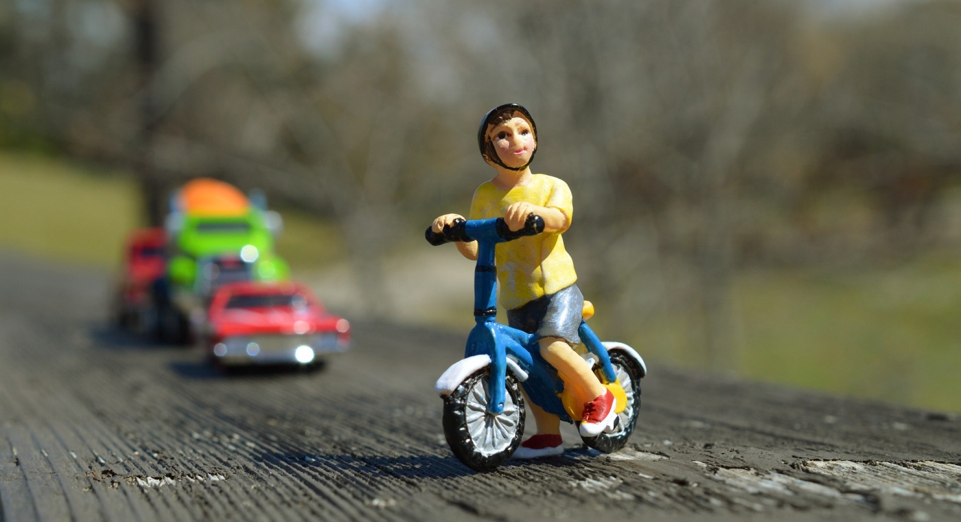 una miniatura fatta a mano ritrae un ciclista in sella alla sua bicicletta e sullo sfondo dei veicoli a motore
